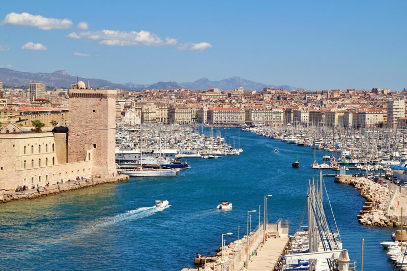 Aerial-view-of-Marseilles-Old-Port-with-water-boats-historic-buildings-and-the-city-in-the-distance