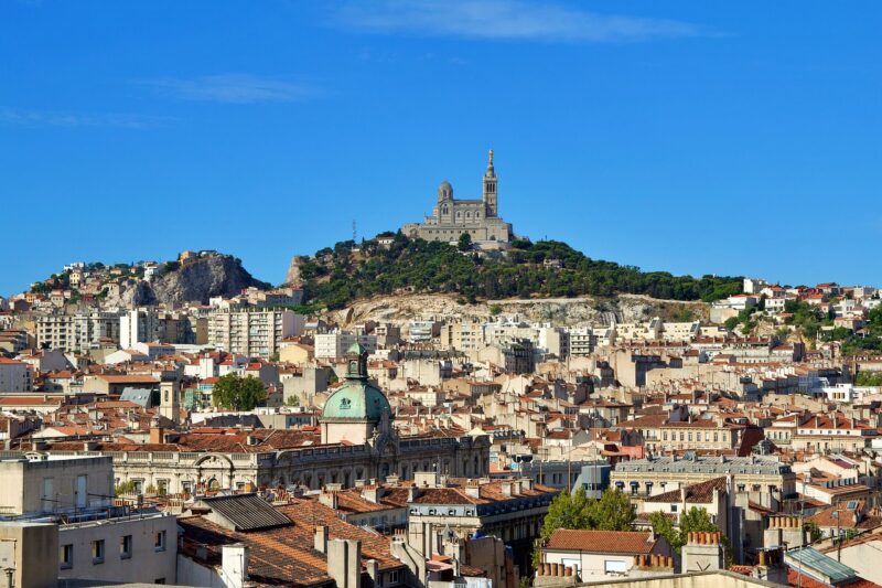 View of the city of Marseille, France with the Basilique Notre Dame de la Garde perched atop a hill in the back and bright blue skies