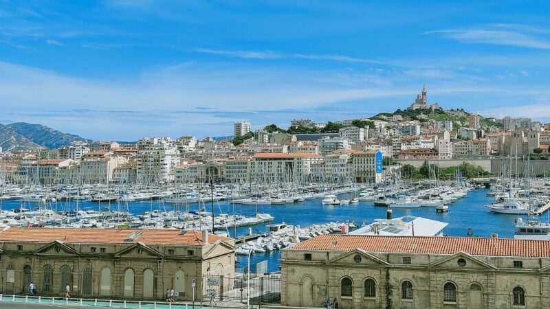 View of the city of Marseille including the port and boats, historic buildings, cathedral on a hill.