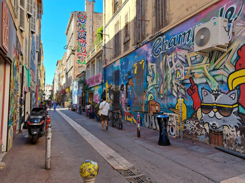 Colorful street art, murals, and graffiti lining both sides of a narrow street in Marseille, France. Despite the travel myth of Marseille being unsafe, this graffiti lined street is safe to walk down.