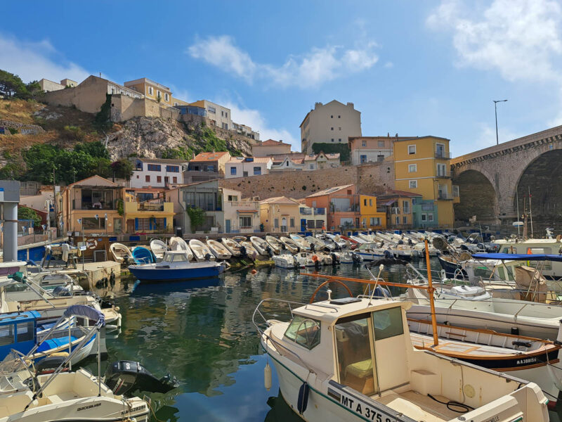 A view of the Vallon des Auffes, a little traditional fishing haven in Marseille in the 7th arrondissement of Marseille. Colorful houses line the hillside with boats in the bay.